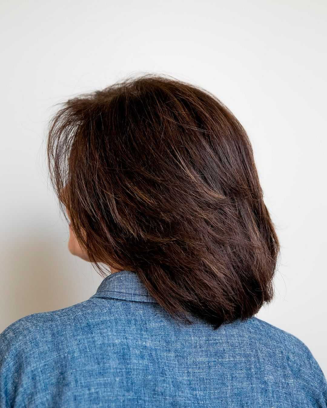 Woman with short, wavy brown hair wearing a blue denim shirt, back view.